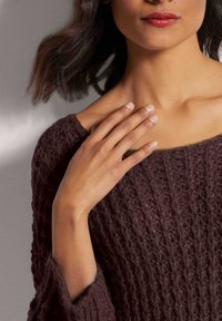 Brauner Strickpullover mit strukturiertem Muster, weitem Ausschnitt und lockeren Ärmeln. Die Hand des Models ruht sanft auf der Schulter.