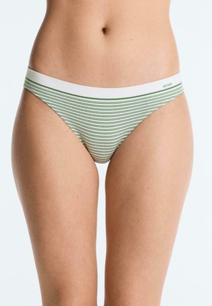 Femeie purtând lenjerie hipster albă cu dungi verzi, cu talie joasă și un mic logo „OYSHO” pe banda din talie.