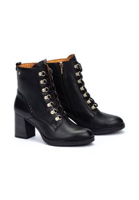 Botas de cuero negras hasta el tobillo con un tacón grueso, detalles dorados, cordones frontales y un zipper lateral, que presentan un detalle trenzado en el tacón.