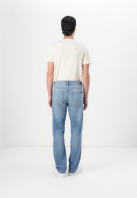 Camiseta corta de manga en color beige claro combinada con jeans de mezclilla azul, patrón desvanecido, ajuste relajado y zapatillas blancas, vista desde atrás.