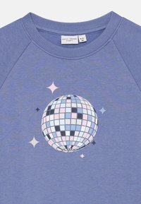 Sweatshirt roxo com um design de bola de discoteca colorido impressa com estrelas, sobre um fundo de tecido suave. Etiqueta Basic Needs visível.