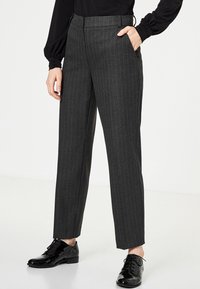 Šedé proužkované kalhoty s rovnými nohavicemi, vyrobené z texturované látky. Obsahují boční kapsy a plochý pas, v kombinaci s černými botami.