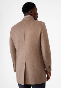 Bruine wollen jas met een gestructureerd ontwerp, een ingestikte kraag en een rugventilatie. De mouwen hebben knoopaccenten voor de sluiting.