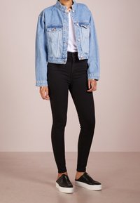 Světle modrá džínová bunda s krátkým střihem, dvěma předními kapsami a stojáčkovým límcem, kombinovaná s vysokými černými skinny džíny a černými slip-on botami.