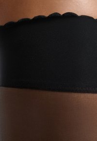 Zwarte en bruine sheer panty’s met een getextureerde bovenband met een golvende rand. De mix van materialen zorgt voor soepele overgangen tussen de kleuren.
