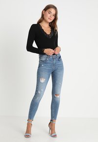 Fekete, hosszú ujjú bodysuit, csipkés díszítéssel, kopott világoskék skinny farmerral és égszínkék, pántos magassarkúval párosítva.