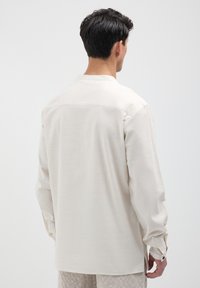 Beige Langarmhemd mit weicher Textur, ausgestattet mit einer Rückenpasse und geknöpften Manschetten. Schlichtes Design ohne Muster oder zusätzliche Akzente.