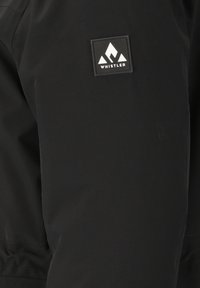 Zwarte jas met een gladde textuur, voorzien van een rechthoekige zwarte patch met het label "WHISTLER" en een wit berglogo op de linkerarm.