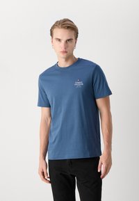 T-shirt in cotone blu con maniche corte e scollatura a girocollo. Presenta un piccolo logo ricamato sul petto. Texture liscia.