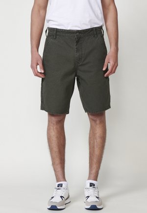 Pantalones cortos de carga verde oscuro con corte recto, que presentan bolsillos laterales y cierre de botón, combinados con zapatillas blancas para un look informal.