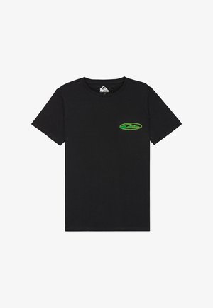 Jeune garçon debout, les mains sur les hanches, portant un t-shirt noir avec un logo vert, un short en jean, des chaussettes blanches rayées et des baskets noires.