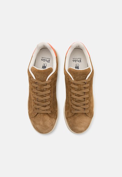 Tenisi din suede maro cu accente portocalii, șireturi plate, guler căptușit și un logo pe limbă. Talpa este de culoare crem și plată.