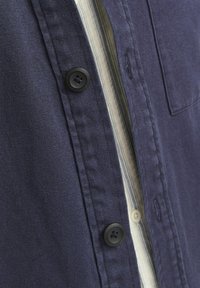Camisa de botones azul marino con botones negros, un bolsillo en el pecho y un forro interior a rayas. Confeccionada en una tela resistente con un acabado texturizado.