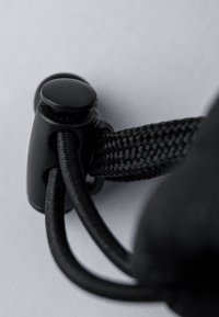 Schwarzer Stoffzug mit geflochtener Textur und rundem Kunststoffstopper. Verfügt über glatte, glänzende Beschläge für eine einfache Anpassung.