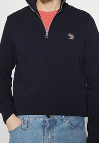 Pullover navy con colletto a zip a un quarto, caratterizzato da un logo di cavallo ricamato colorato sul petto, realizzato in tessuto morbido. Vestibilità casual.