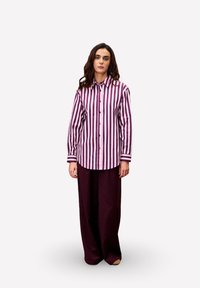 Gestreepte button-up shirt in paars en wit met lange mouwen; gecombineerd met wijde paarse broek. Glad materiaal met een klassieke kraag.