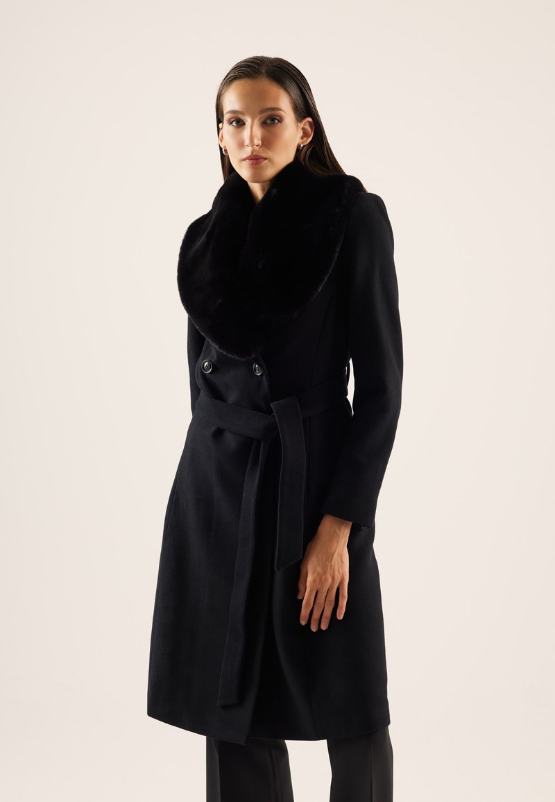 Cappotto in misto lana nero con un ampio colletto in pelliccia sintetica nera, bottoni doppi, e una cintura annodata in vita, caratterizzato da maniche lunghe e una linea dritta.