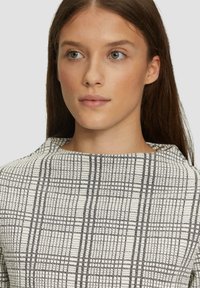 Witte en zwarte blouse met een patroon die een hoge halslijn en een gestructureerde stof met een ruitontwerp heeft, en een moderne, gestructureerde silhouet biedt.