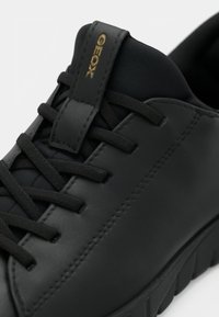 Μαύρο δερμάτινο αθλητικό παπούτσι με δέσιμο κορδονιών, με υφή στην επιφάνεια και χρυσό λογότυπο στη γλώσσα. Ανθεκτική σόλα από καουτσούκ.