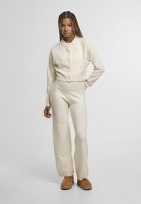 Kremowy sweter robiony na drutach z okrągłym dekoltem i zapięciem na guziki, zestawiony z pasującymi spodniami typu wide-leg i brązowymi zamszowymi butami na platformie.