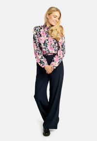 Kwiecista bluzka z długim rękawem w różowo-zielone wzory, zestawiona z granatowymi, szerokimi spodniami o wysokim stanie. Gładki materiał, luźny krój.