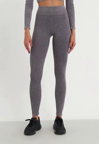 Leggings cinzentos canelados com cintura alta, feitos de material elástico, combinados com ténis desportivos pretos, em pé sobre um fundo neutro.