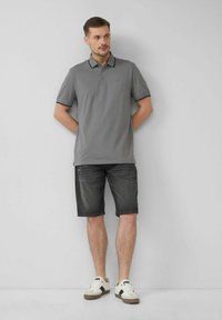 Graues Poloshirt mit Kragen und zwei Knöpfen, kombiniert mit dunklen Jeansshorts. Abgerundet mit weißen Sneakern mit schwarzen Akzenten.