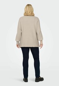 Beige ribbed sweater with long, puffed sleeves, dropped shoulder seams, and a curved hem, paired with dark slim-fit jeans and black shoes.