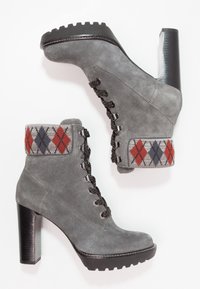 Bottines en daim gris avec un haut talon noir, design à lacets et bord en tricot à motif argyle rouge et bleu. Surface texturée et semelle robuste.