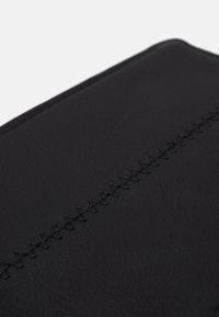 Materiale in pelle nera con una cucitura visibile lungo il centro. Texture liscia con una finitura opaca.