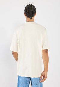 Lys beige kortermet t-skjorte med avslappet passform, laget av myk stoff, med rund hals og en enkel, glatt tekstur.