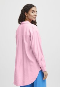 Rosa Langarmhemd mit lockerer Passform, strukturiertem Stoff, geknöpften Manschetten und abgerundetem Saum, getragen über blauen Hosen.