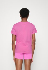 Růžové tričko s kulatým výstřihem, krátkými rukávy a hladkou texturou, spárované s odpovídajícími růžovými šortkami, viděné ze zadní strany.