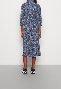 Modrá šaty s květinovým vzorem, s rukávy o třičtvrtě a středně dlouhým lemem. Nosené s černými teniskami s bílou hvězdou.