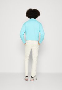 Pullover azzurro chiaro con colletto alto, abbinato a pantaloni color crema. Scarpe da ginnastica grigie con dettagli rossi e marchio nero.