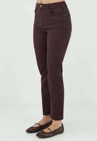 Jeans bordeaux con una vestibilità slim, vita alta e tasche anteriori. Abbinati a flats neri intrecciati con dettagli delle cinghie. Texture liscia.