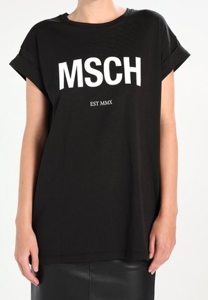 Personne portant un t-shirt noir à manches retroussées avec le texte blanc "MSCH EST MMX" sur le devant, associé à une jupe noire.