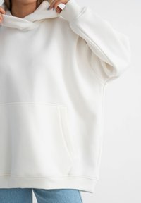 Felpa bianca con tasca anteriore, vestibilità oversize, polsini a coste e cappuccio regolabile con cordino, realizzata in morbido materiale misto cotone.