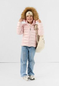 Giacca piumino rosa chiaro con cappuccio foderato in pelliccia, abbinata a jeans in denim azzurro e uno zaino beige. Sneakers bianche completano il look.
