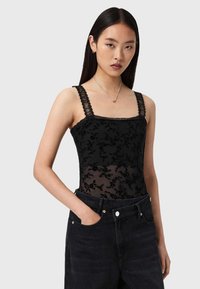Schwarzer Bodysuit mit floraler Spitzenüberlagerung, quadratischem Ausschnitt, breiten Spitzen-Trägern und transparentem unteren Bereich, kombiniert mit hoch taillierten schwarzen Jeans.