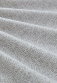 Lichtgrijze stof met een zachte, gestructureerde oppervlakte, die subtiele variaties en plooien vertoont, geschikt voor bekleding of kleding.