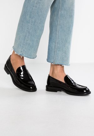 Czarne lakierowane mokasyny o gładkim wykończeniu, płaskiej podeszwie i dekoracyjnym pasku z przodu, zestawione z jasnoniebieskimi skrojonymi dżinsami.