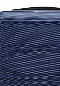 Valigia rigida di colore blu navy, con una superficie testurizzata che presenta un motivo esagonale e cinghie incassate per una maggiore durabilità.