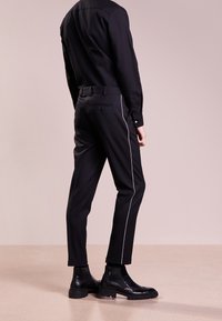 Svarta skräddarsydda byxor med slim fit, vit sidestreck och en bakfickdetalj, matchat med kraftiga svarta ankelstövlar.