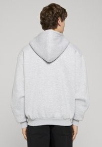 Svetlo šedý mikina s kapucňou a voľným strihom, pružnými manžetami a lemom. Tkanina má jemnú textúru a obsahuje veľkú kapucňu na zadnej strane.