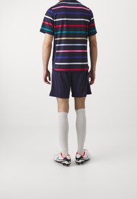 Sports kit featuring a navy short-sleeve shirt with horizontal stripes in pink, teal, and purple, paired with navy shorts and white socks.