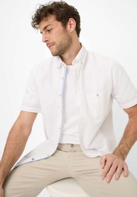Witte kortekmouw button-up shirt met een subtiele textuur, lichtblauwe gestreepte binnenplacket en een enkele borstzak. Beige broek.