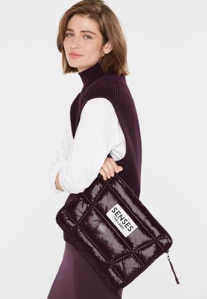 Gepolsterte dunkelpurpurrote Clutch mit geometrischer Steppnaht und einem Reißverschluss. Verfügt über ein weißes Etikett mit der Aufschrift "SENSES THE LABEL." Glatte, glänzende Textur.