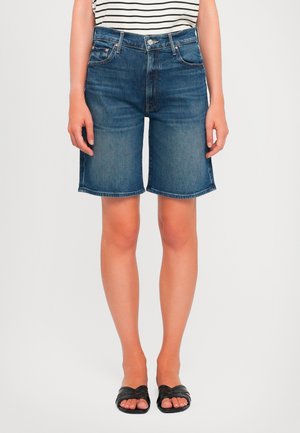 Denim Bermuda shorts in dark blue with a straight cut, five pockets, and a button fly. Paired with a black and white striped shirt and sandals.