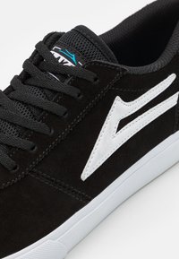 Black suede sneaker with white accents and logo, featuring a textured upper, lace-up design, and rubber sole.